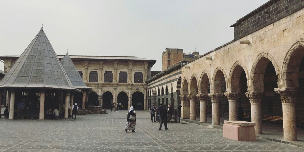 a group of people walking around a courtyard with buildings in the background